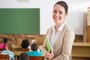 Pretty teacher smiling at camera at back of classroom at the elementary school